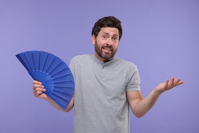 Confused man holding hand fan on purple background