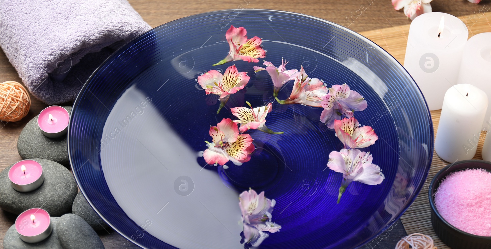 Photo of Bowl of water with flowers and different spa supplies on wooden table