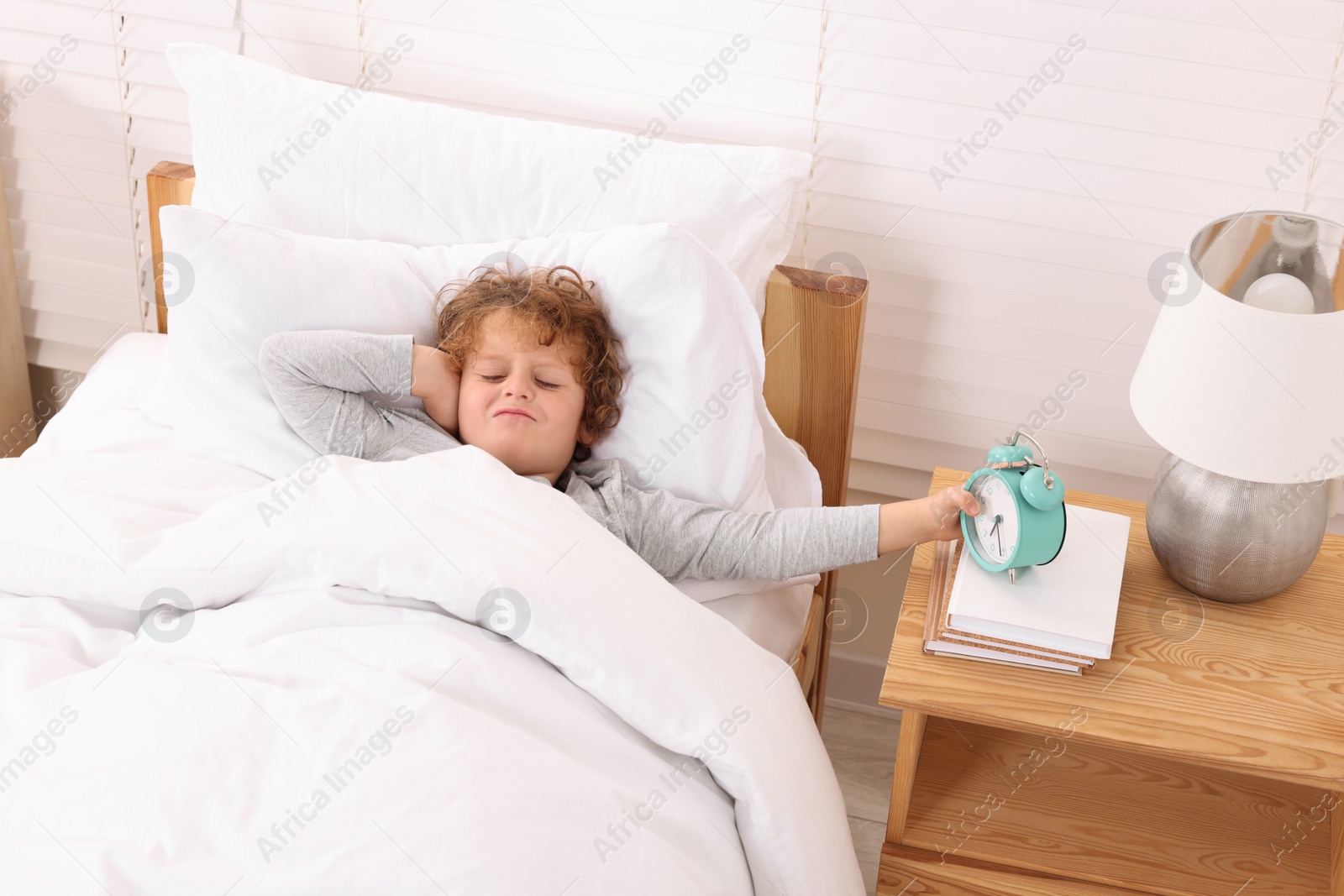 Photo of Sad little boy with alarm clock in bedroom