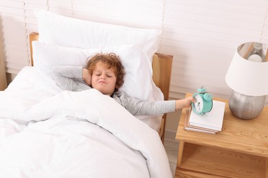 Sad little boy with alarm clock in bedroom