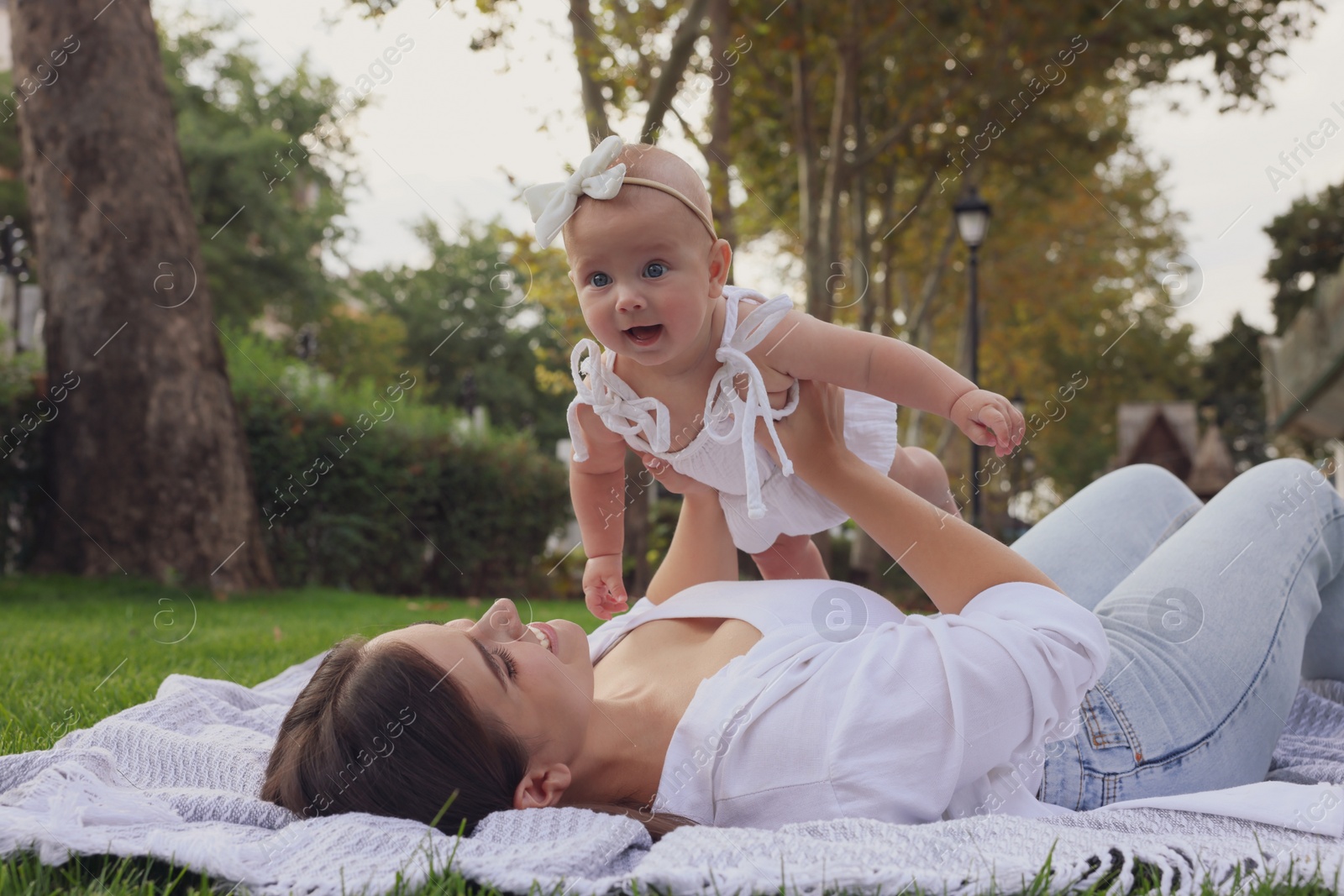 Photo of Happy mother with adorable baby lying on green grass in park