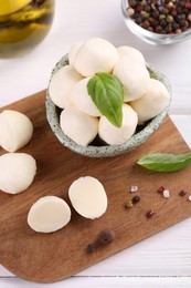 Photo of Tasty mozzarella balls, basil leaves and spices on white wooden table, above view