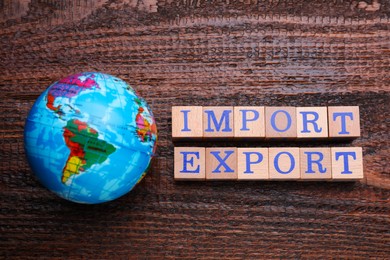 Photo of Words Import and Export made of cubes and globe on wooden table, flat lay