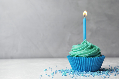 Delicious birthday cupcake with cream and burning candle on table. Space for text