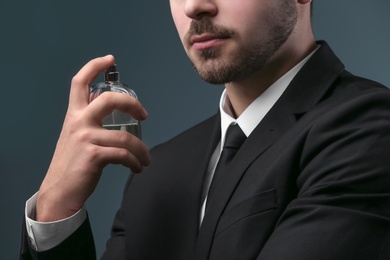 Photo of Handsome man in suit using perfume on dark background, closeup