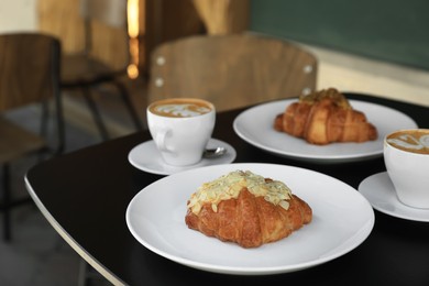 Photo of Tasty croissants and cups of aromatic coffee on black table in cafeteria