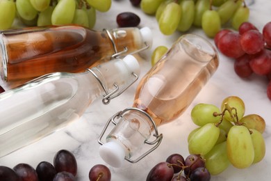 Photo of Different types of vinegar in bottles and grapes on light table, closeup