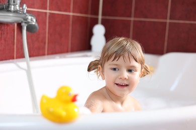 Photo of Smiling girl bathing with toy duck in tub at home, selective focus