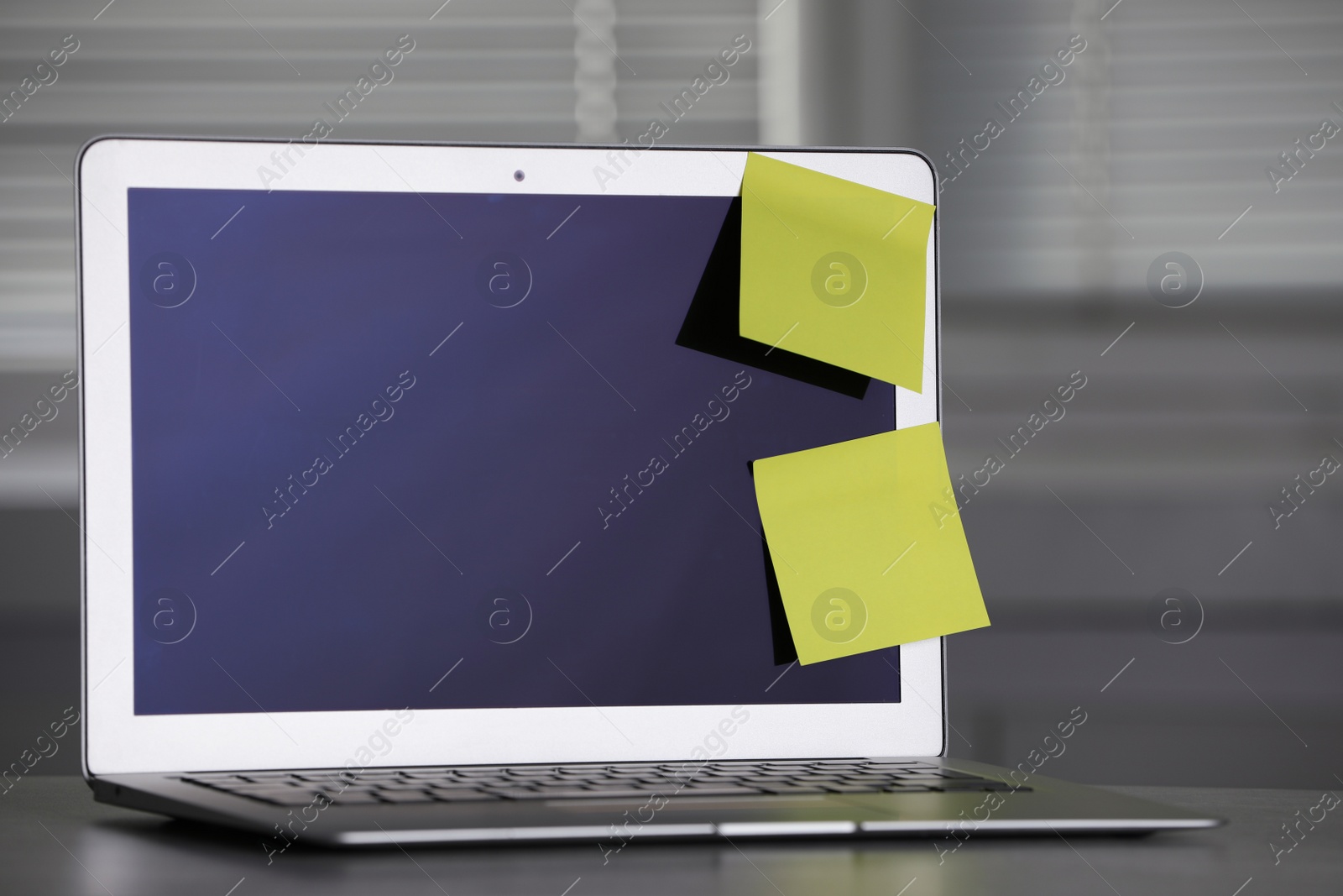 Photo of Laptop with blank sticky notes on grey office desk. Space for text