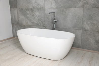 Photo of Stylish ceramic tub near light grey tiled wall indoors