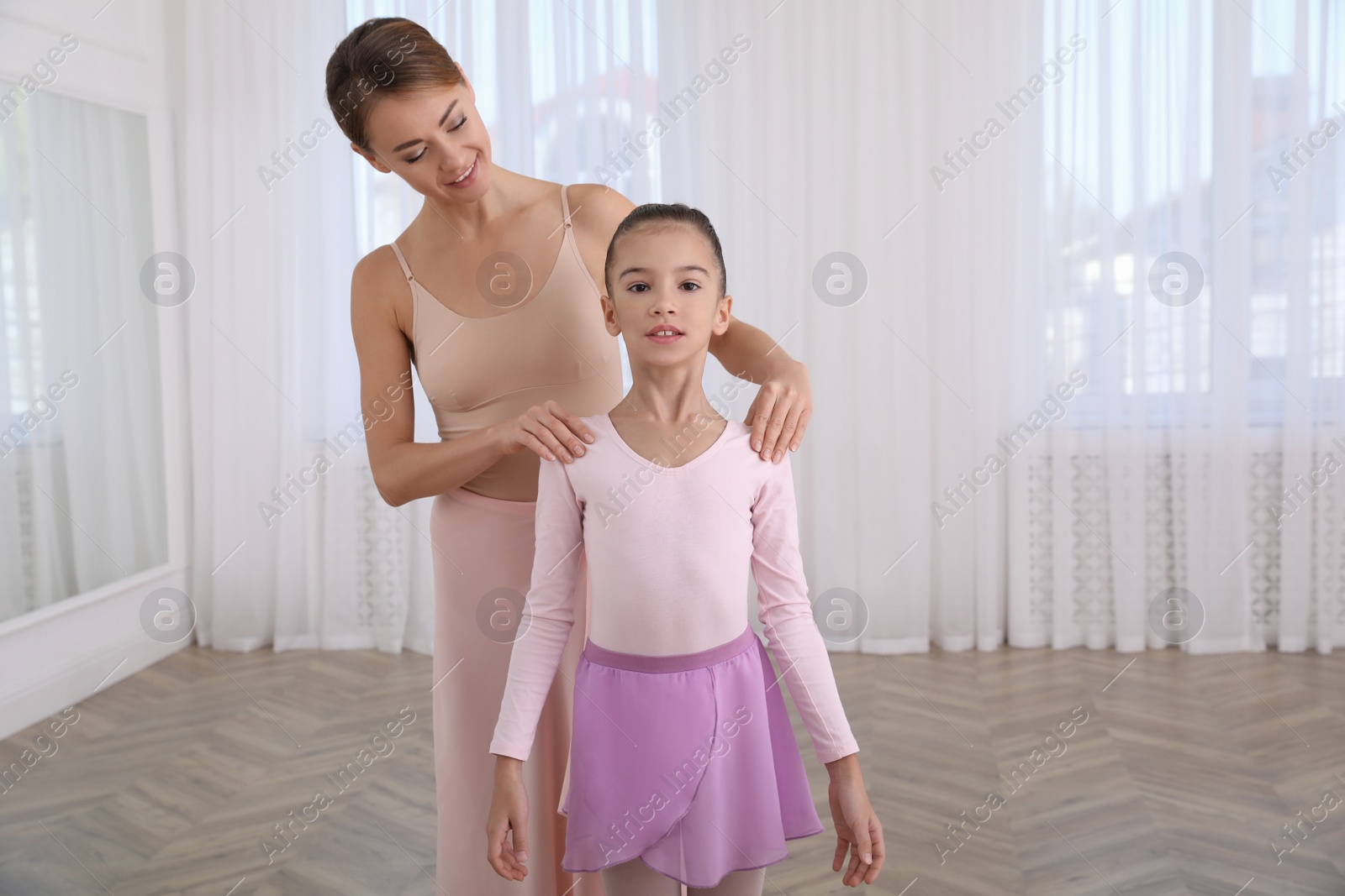 Photo of Ballet teacher fixing little girl's posture in studio. Space for text