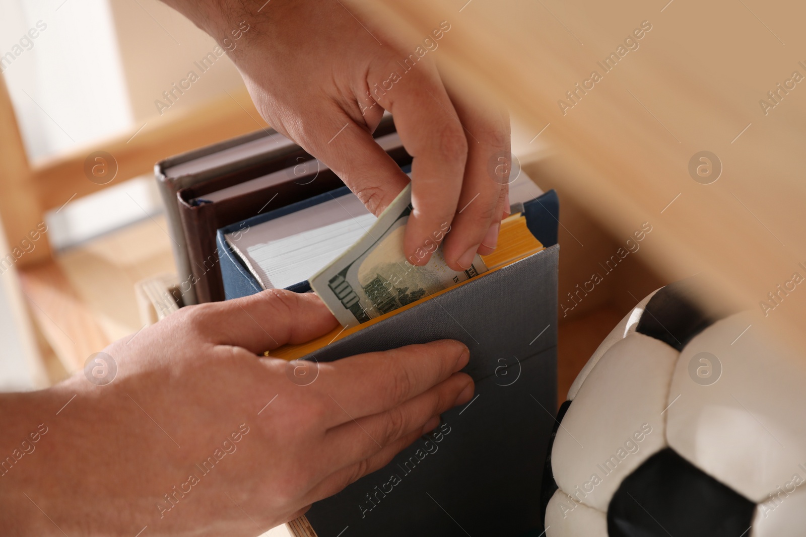 Photo of Man hiding money in book indoors, closeup. Financial savings