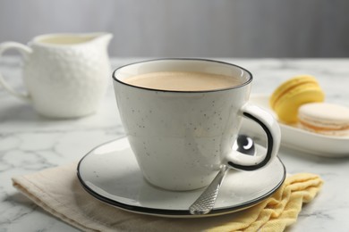 Photo of Tasty cappuccino in cup, spoon and saucer on white marble table, closeup