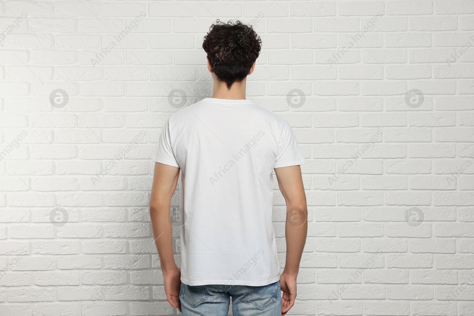 Photo of Man wearing stylish t-shirt near white brick wall, back view. Mockup for design