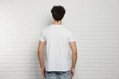 Man wearing stylish t-shirt near white brick wall, back view. Mockup for design