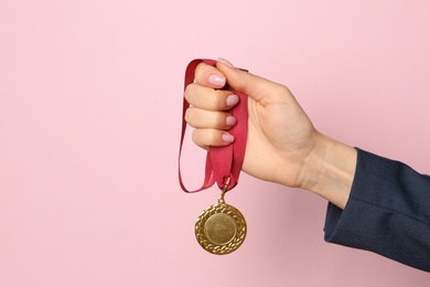 Photo of Woman holding golden medal on color background, closeup. Space for text