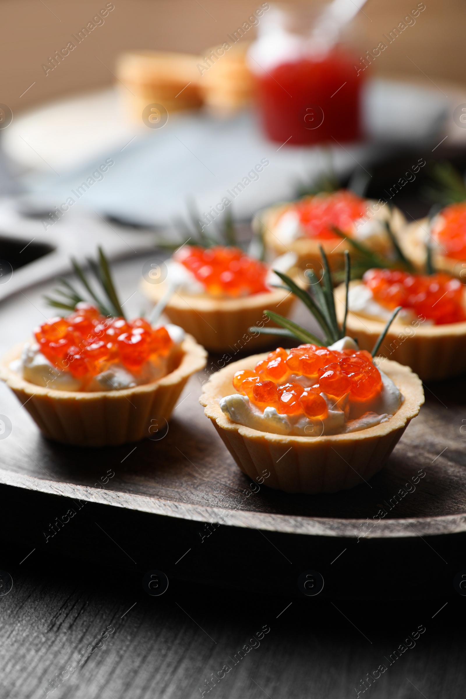 Photo of Delicious tartlets with red caviar and cream cheese served on wooden table, closeup