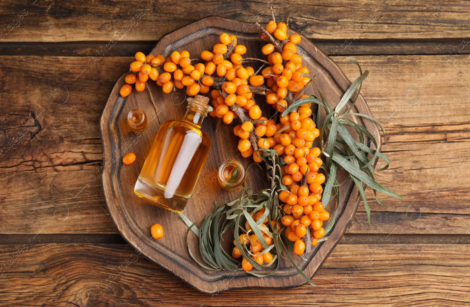 Photo of Natural sea buckthorn oil and fresh berries on wooden table, top view