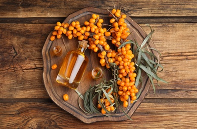 Photo of Natural sea buckthorn oil and fresh berries on wooden table, top view