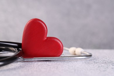 Photo of Stethoscope and red heart on grey stone table, closeup. Space for text