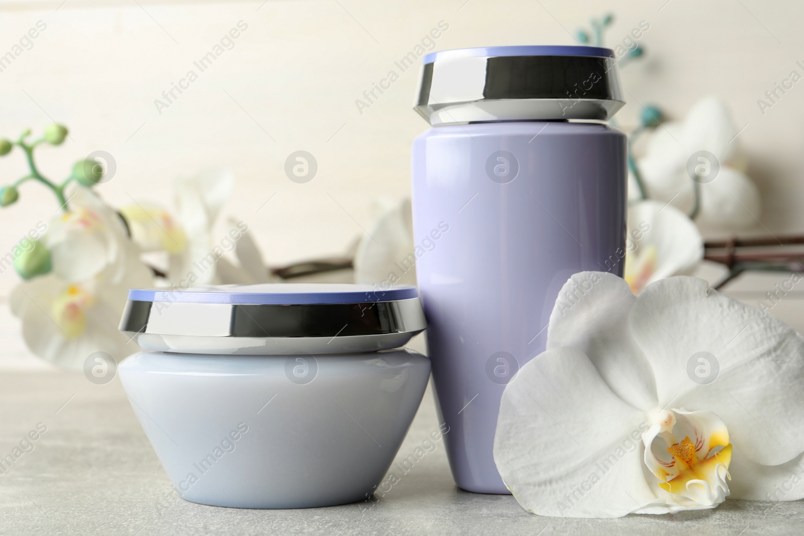 Photo of Hair care cosmetic products and orchid flower on grey table