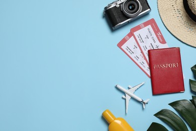Photo of Passport with tickets, airplane model, camera, hat, sunscreen and tropical leaves on light blue background, flat lay. Space for text