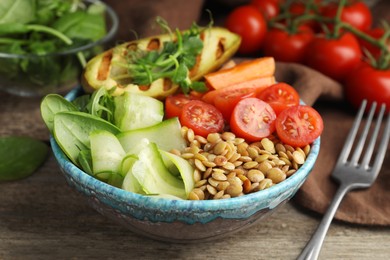 Delicious lentil bowl with avocado, tomatoes and cucumber on wooden table