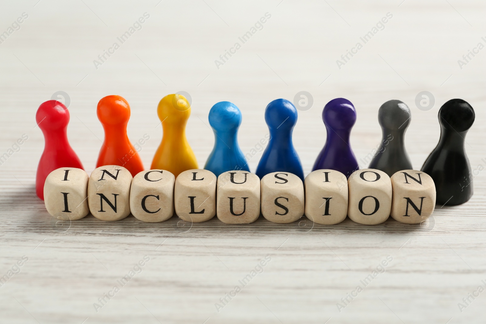 Photo of Colorful pawns and cubes with word Inclusion on white wooden table, closeup