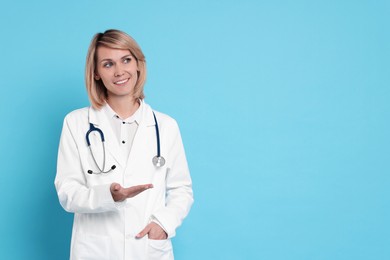 Photo of Smiling doctor holding something on light blue background. Space for text