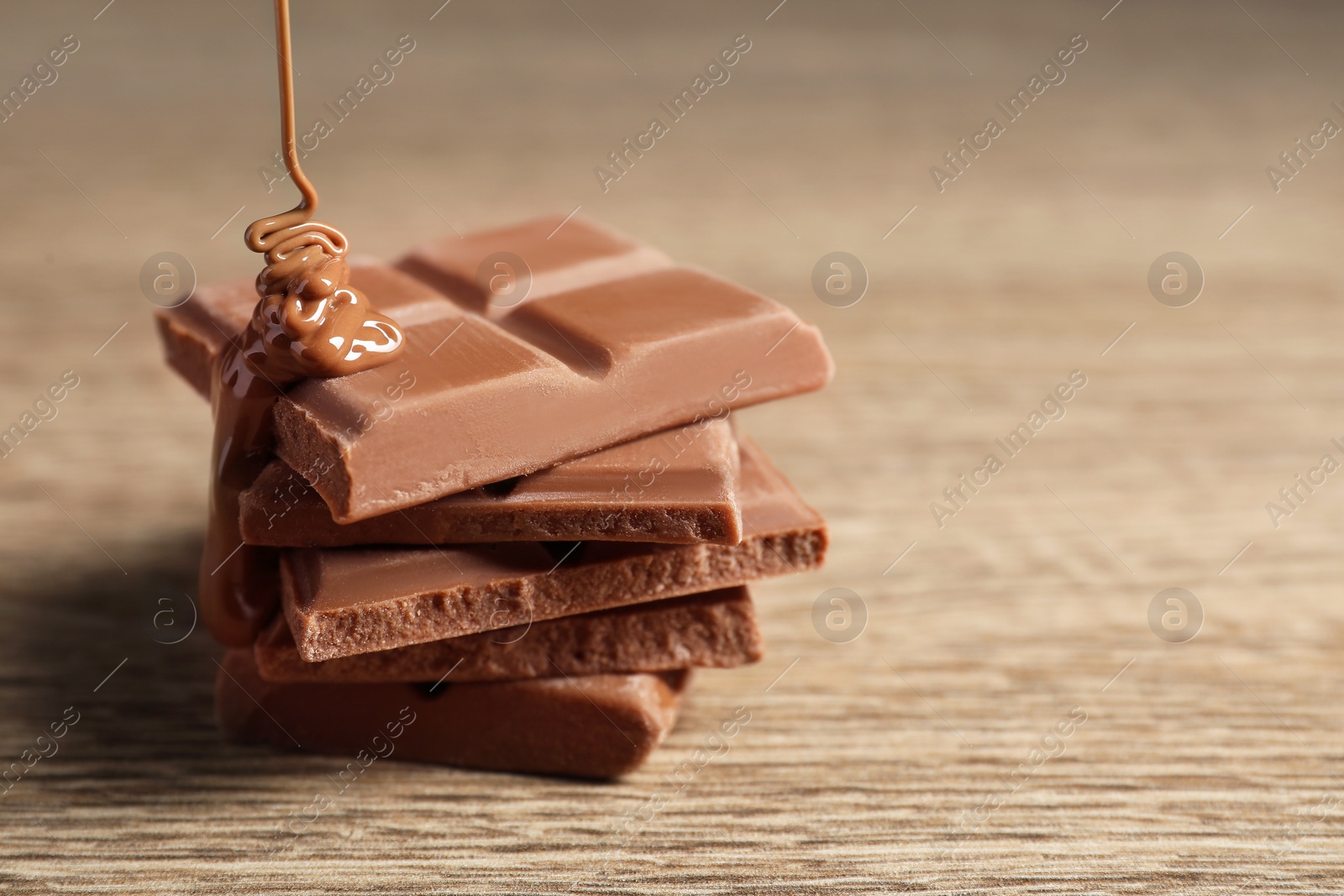 Photo of Pouring tasty milk chocolate paste onto pieces on wooden table, closeup. Space for text