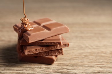 Photo of Pouring tasty milk chocolate paste onto pieces on wooden table, closeup. Space for text