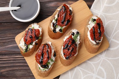 Delicious bruschettas with sun-dried tomatoes, cream cheese and balsamic vinegar on wooden table, flat lay