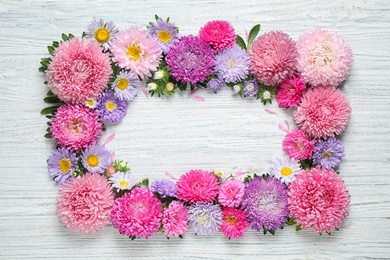 Frame made of beautiful aster flowers on white wooden table. Space for text