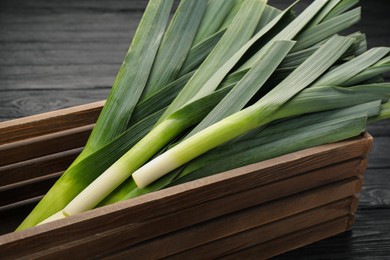 Fresh raw leeks in wooden crate on black table, closeup