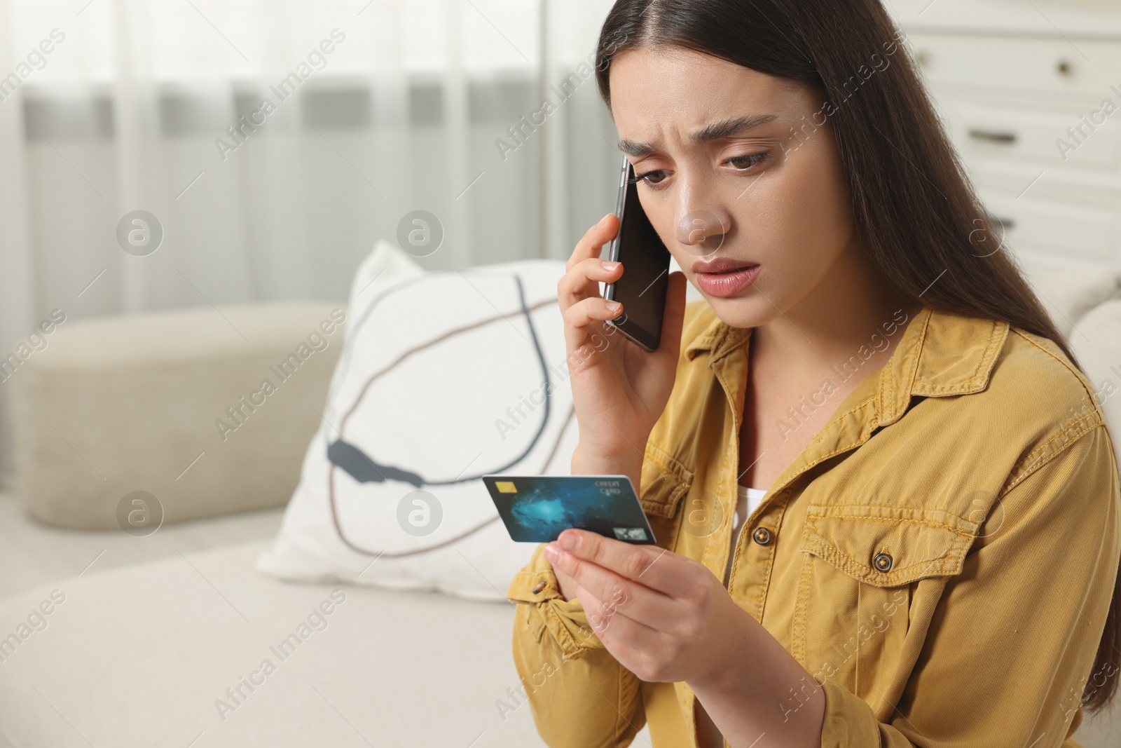 Photo of Confused woman with credit card talking on phone at home, space for text. Be careful - fraud