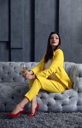 Beautiful businesswoman with glass of champagne on sofa indoors. Luxury lifestyle