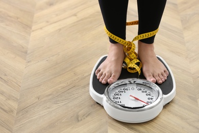 Photo of Closeup view of woman tied with measuring tape using scale on floor, space for text. Overweight problem after New Year party