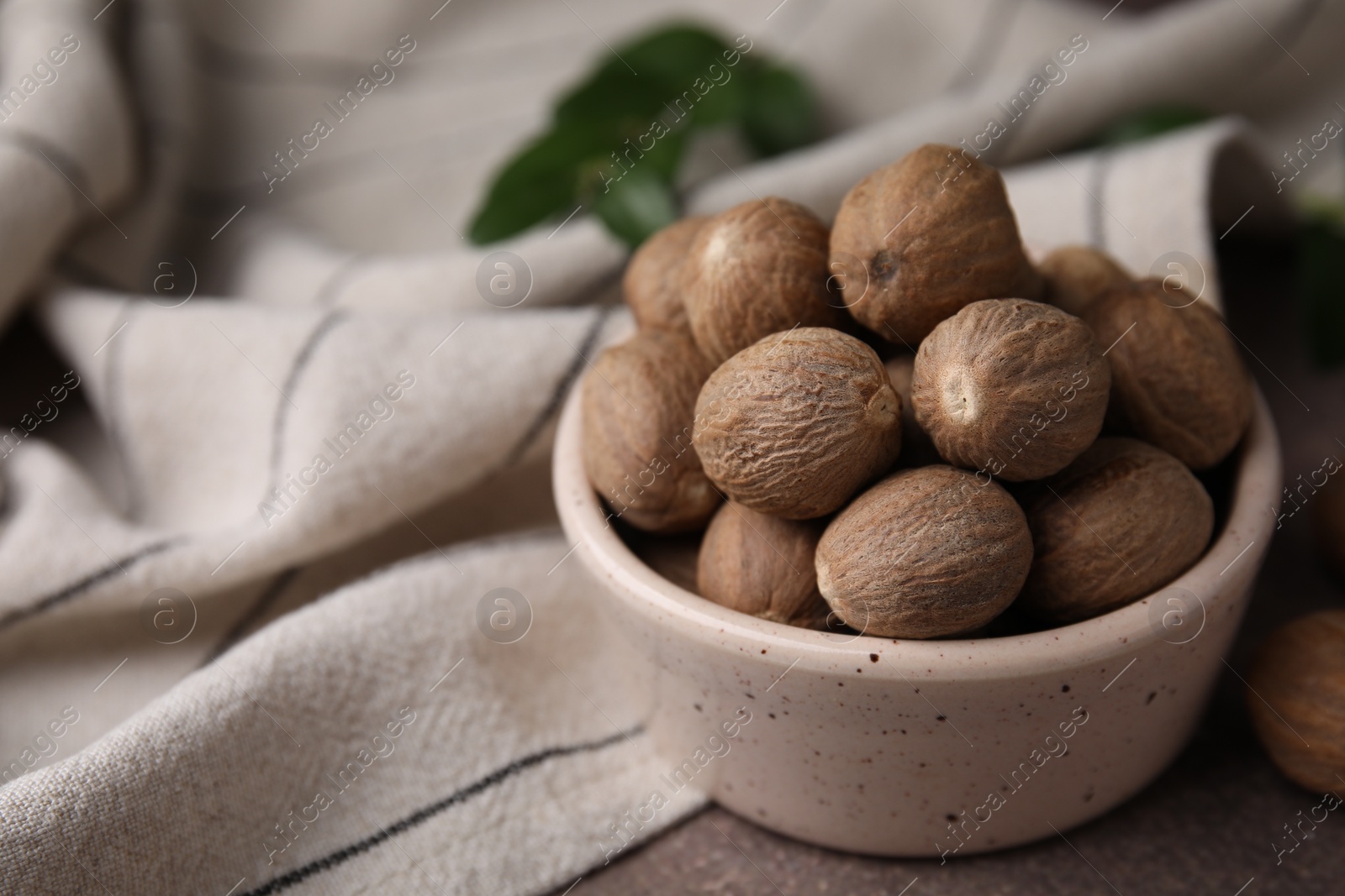 Photo of Whole nutmegs in bowl on brown table, closeup. Space for text