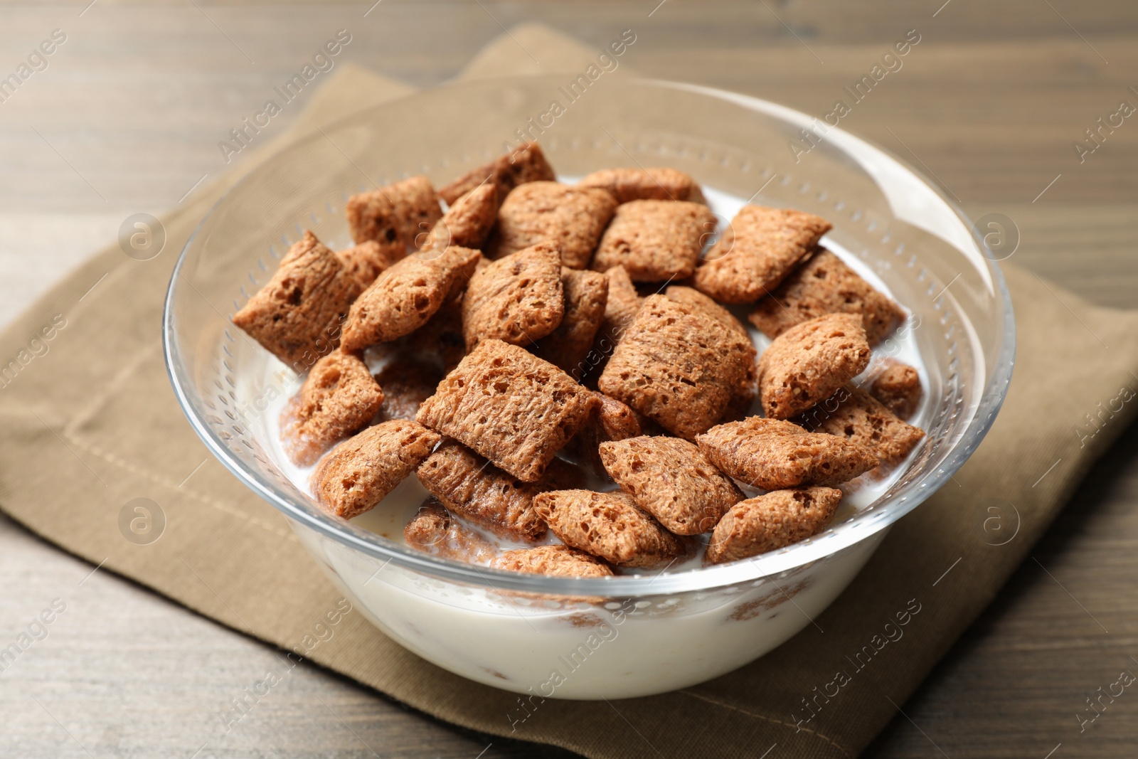 Photo of Tasty corn pads with milk in glass bowl on wooden table, closeup