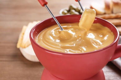 Dipping bread into pot with cheese fondue on table, closeup