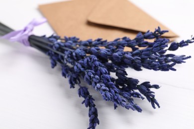 Photo of Bouquet of beautiful preserved lavender flowers and envelope on white wooden table, closeup