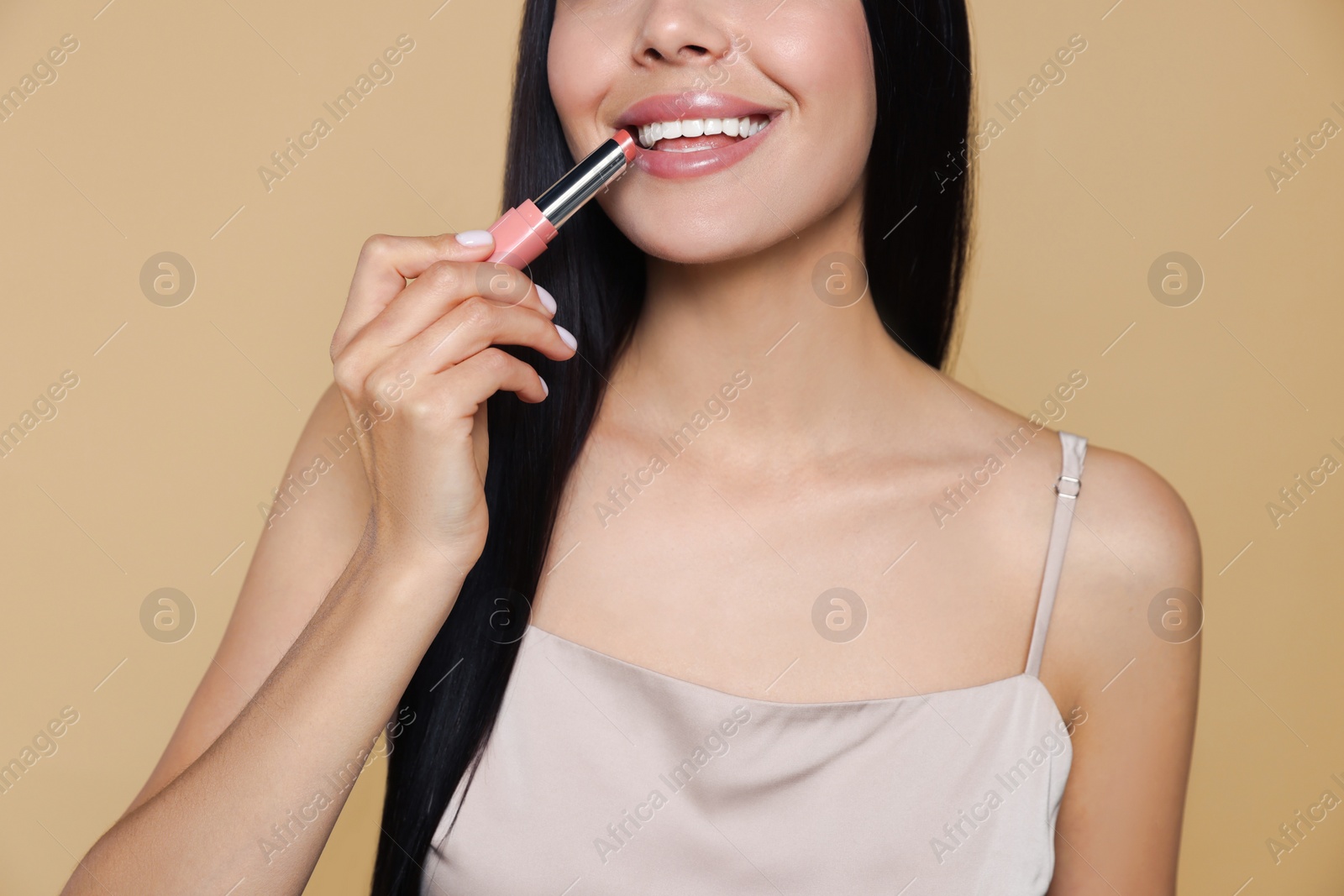 Photo of Young woman applying nude lipstick on beige background, closeup