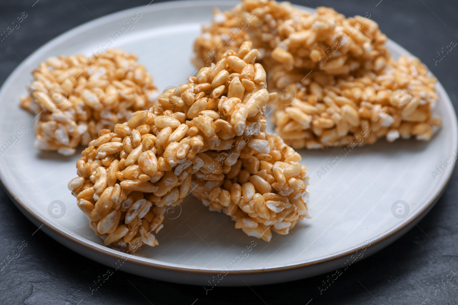 Photo of Plate with puffed rice pieces (kozinaki) on black table, closeup