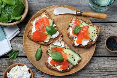 Photo of Delicious sandwiches with cream cheese, salmon, cucumber and spinach served on wooden table, flat lay