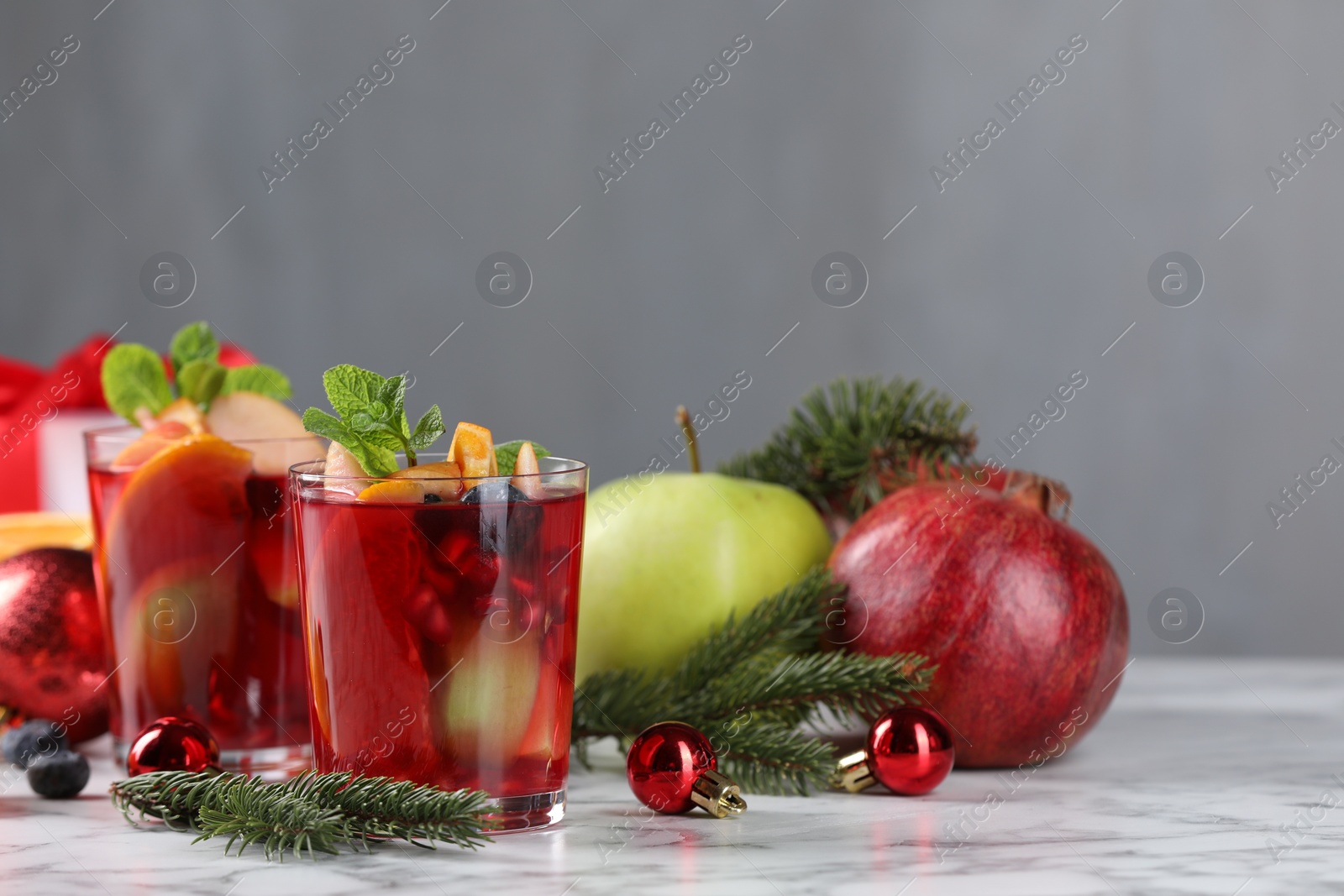 Photo of Aromatic Sangria drink in glasses, ingredients and Christmas decor on white marble table