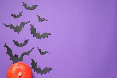 Flat lay composition with pumpkin and paper bats on purple background, space for text. Halloween decor