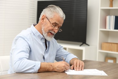 Senior man signing Last Will and Testament at wooden table indoors. Space for text