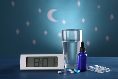 Photo of Digital alarm clock and different remedies for insomnia treatment near glass of water on table against blue wall decorated with stars and crescent