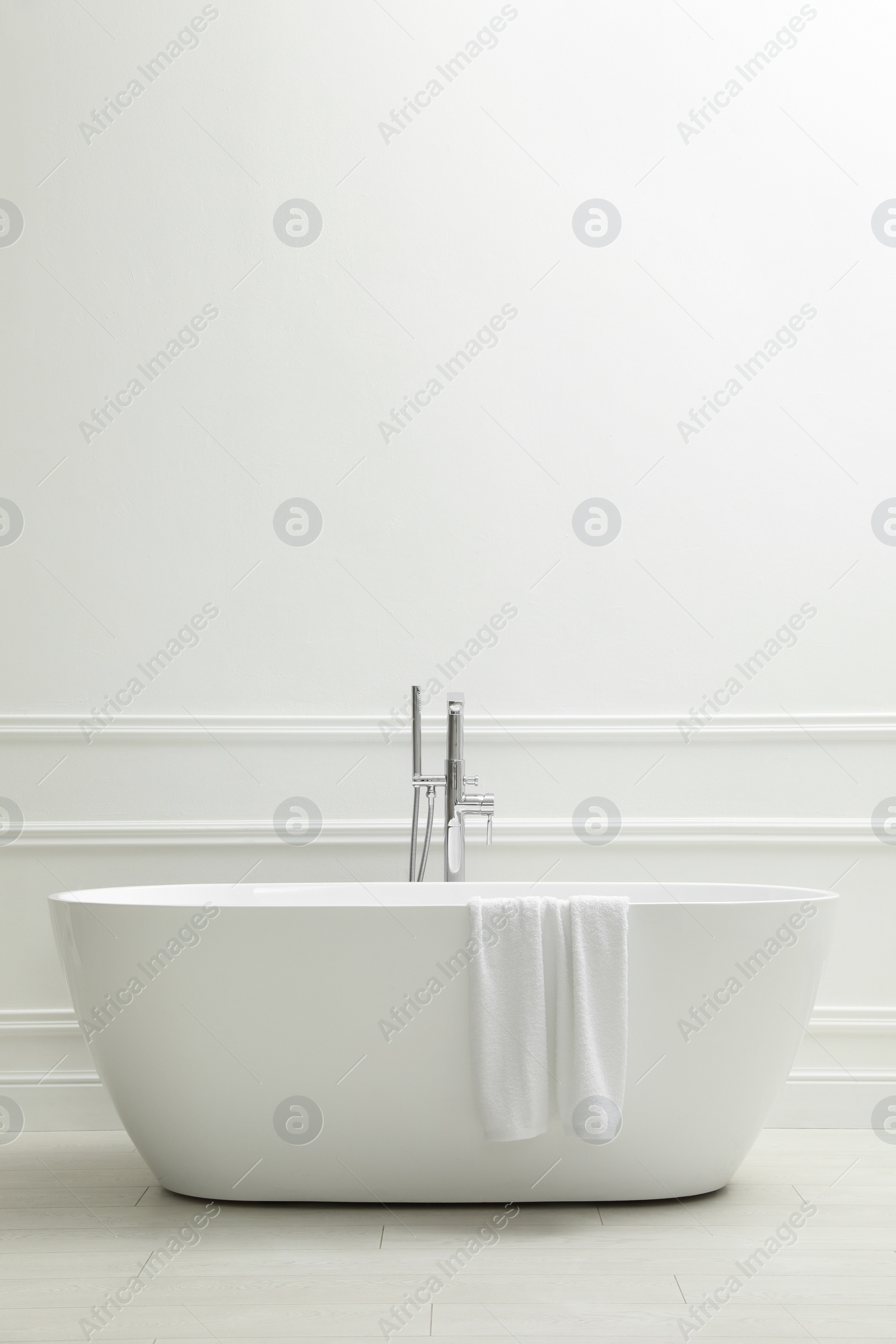 Photo of Modern ceramic bathtub with towel near white wall indoors, space for text