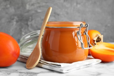 Photo of Delicious persimmon jam and fresh fruits on white marble table, closeup